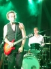 In grünes Licht getauchtes Foto, REINAUER im Vordergrund mit E-Gitarre singt ins Mikrofon, im Hintergrund Jens Gerö am Schlagzeug